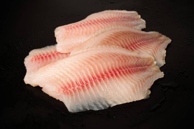 Siyah arkaplanda taze tilapia filetosu, üst görünüm. 