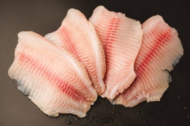 Siyah arkaplanda taze tilapia filetosu, üst görünüm. 