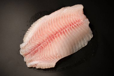 Siyah arkaplanda taze tilapia filetosu, üst görünüm. 