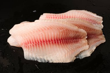 Siyah arkaplanda taze tilapia filetosu, üst görünüm. 