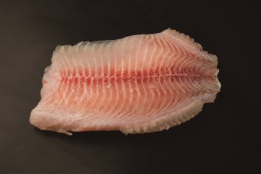 Siyah arkaplanda taze tilapia filetosu, üst görünüm. 