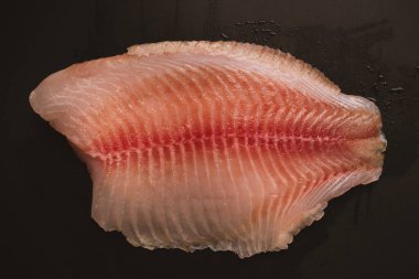 Siyah arkaplanda taze tilapia filetosu, üst görünüm. 