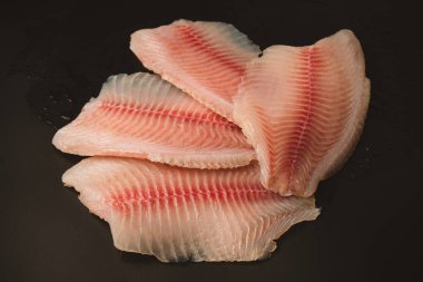 Siyah arkaplanda taze tilapia filetosu, üst görünüm. 