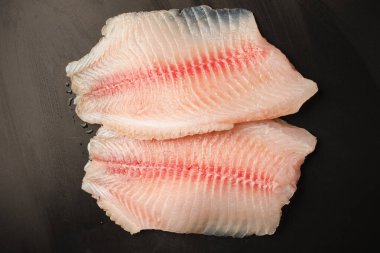 Siyah arkaplanda taze tilapia filetosu, üst görünüm. 