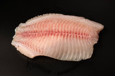 Siyah arkaplanda taze tilapia filetosu, üst görünüm. 