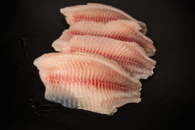 Siyah arkaplanda taze tilapia filetosu, üst görünüm. 