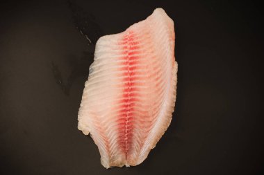 Siyah arkaplanda taze tilapia filetosu, üst görünüm. 