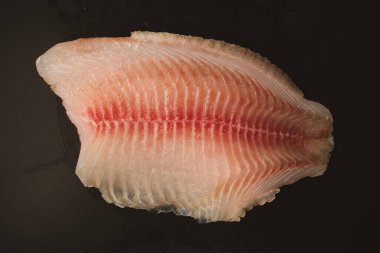 Siyah arkaplanda taze tilapia filetosu, üst görünüm. 