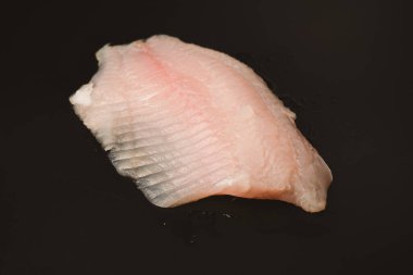 Siyah arkaplanda taze tilapia filetosu, üst görünüm. 