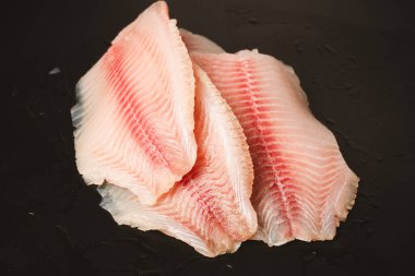 Siyah arkaplanda taze tilapia filetosu, üst görünüm. 