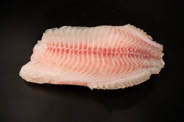Siyah arkaplanda taze tilapia filetosu, üst görünüm. 