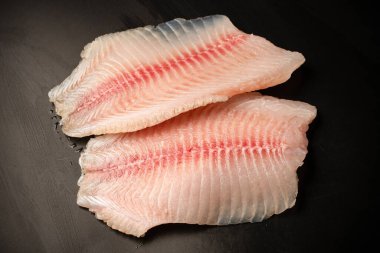 Siyah arkaplanda taze tilapia filetosu, üst görünüm. 