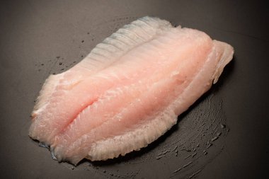 Siyah arkaplanda taze tilapia filetosu, üst görünüm. 