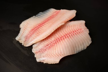 Siyah arkaplanda taze tilapia filetosu, üst görünüm. 