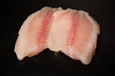 Siyah arkaplanda taze tilapia filetosu, üst görünüm. 