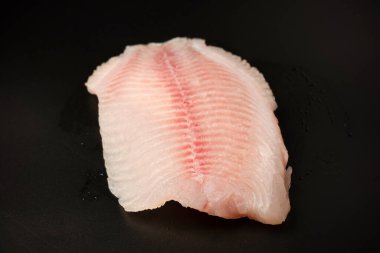 Siyah arkaplanda taze tilapia filetosu, üst görünüm. 