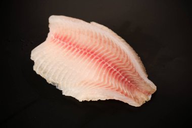 Siyah arkaplanda taze tilapia filetosu, üst görünüm. 