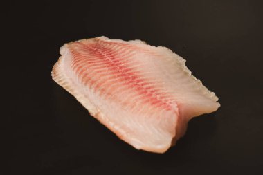 Siyah arkaplanda taze tilapia filetosu, üst görünüm. 