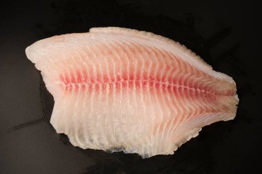 Siyah arkaplanda taze tilapia filetosu, üst görünüm. 