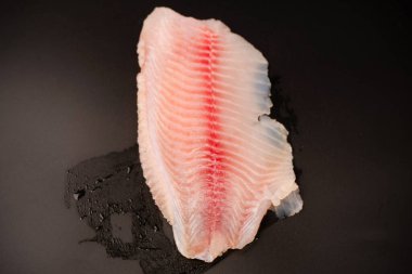 Siyah arkaplanda taze tilapia filetosu, üst görünüm. 