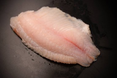 Siyah arkaplanda taze tilapia filetosu, üst görünüm. 