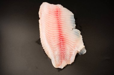 Siyah arkaplanda taze tilapia filetosu, üst görünüm. 