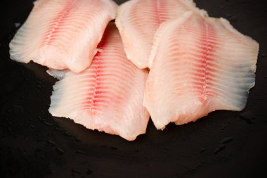Siyah arkaplanda taze tilapia filetosu, üst görünüm. 
