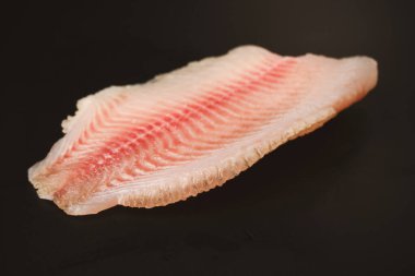 Siyah arkaplanda taze tilapia filetosu, üst görünüm. 