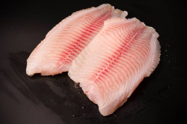 Siyah arkaplanda taze tilapia filetosu, üst görünüm. 