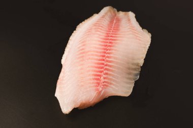 Siyah arkaplanda taze tilapia filetosu, üst görünüm. 