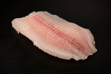 Siyah arkaplanda taze tilapia filetosu, üst görünüm. 