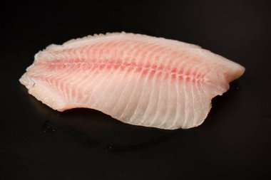 Siyah arkaplanda taze tilapia filetosu, üst görünüm. 