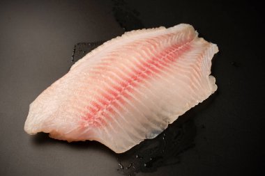 Siyah arkaplanda taze tilapia filetosu, üst görünüm. 