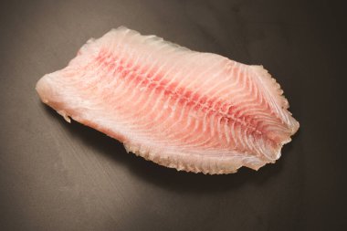 Siyah arkaplanda taze tilapia filetosu, üst görünüm. 