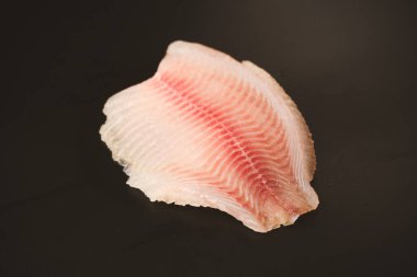 Siyah arkaplanda taze tilapia filetosu, üst görünüm. 