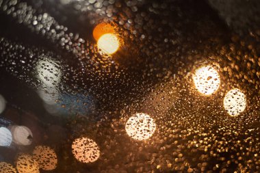 Yağmur damlaları ve ışıklarla bulanık arkaplan.