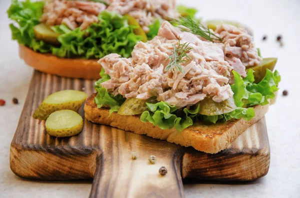 Homemade tuna salad sandwiches on cutting board with pickles aside