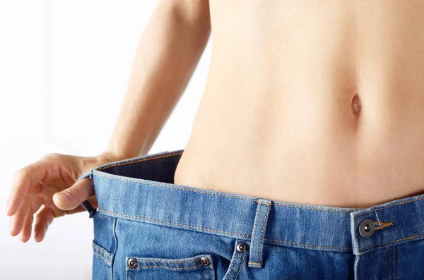 stock image Caucasian female model in blue jeans showing her flat stomach. Weightloss concept.