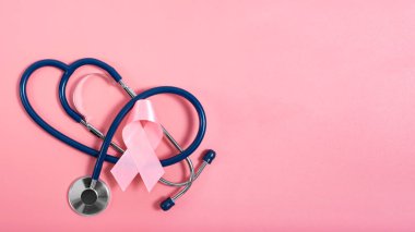 Göğüs kanseri farkındalığı sembolü olarak pembe arka planda steteskop ve pembe kurdele. Düz görünüm