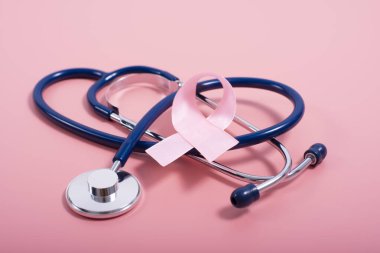 Göğüs kanseri farkındalığı sembolleri olarak pembe arka planda steteskop ve pembe kurdele.