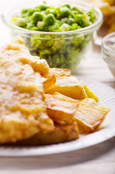 Traditional British street food fish and chips with mushy peas on parchment paper