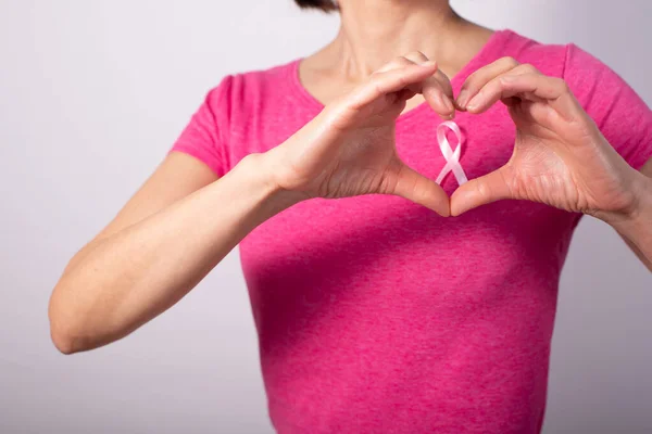 White female model with pink ribbon hold fingers in heart shape