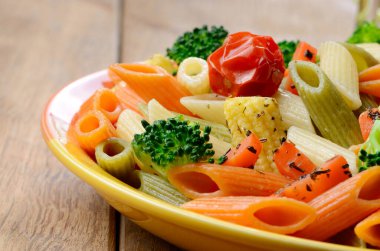 makarna penne brokoli havuç Mısır ve ahşap masa üstünde domates salatası