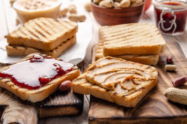 Fıstık ezmeli ve reçelli sandviçleri ekmek dilimleme tahtasının yanında düşük açılı. Sağlıklı yeme kavramı