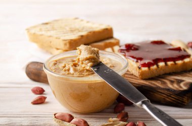 Cam kaseye düşük açılı bir bakış açısı beyaz ahşap masada fıstık ezmesi ve reçel. Sağlıklı yeme kavramı