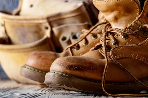 stock image Yellow leather used work boots and tool belt on wooden background closeup. Place for text