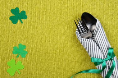 Aziz Patrick Günü düz seti çatal, kaşık ve peçeteyle yeşil bir mindere serilmiş, el yapımı yoncalarla. Kopyalama alanı