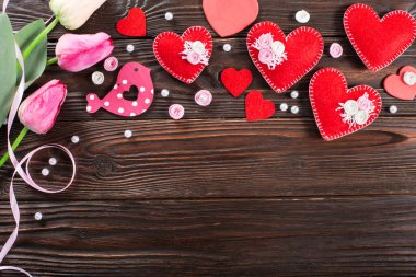 Sewed handmade fabric hearts tulips and ribbon for valentine day on dark wooden background with copy space