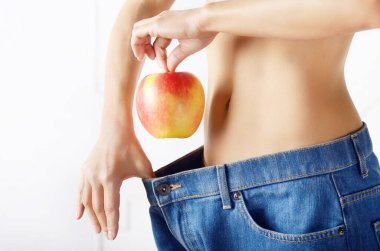 Kırmızı elma onu düz mide gösteren mavi kot beyaz kadın modeli. Sağlıklı yaşam tarzı ve weightloss kavramı.