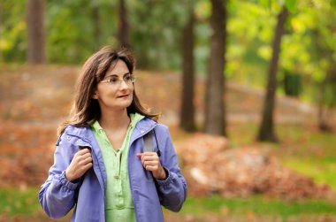 Orta yaşlı beyaz kadın model, sonbahar zamanı ormanda sırt çantasıyla geziyor. Ruh sağlığı konsepti